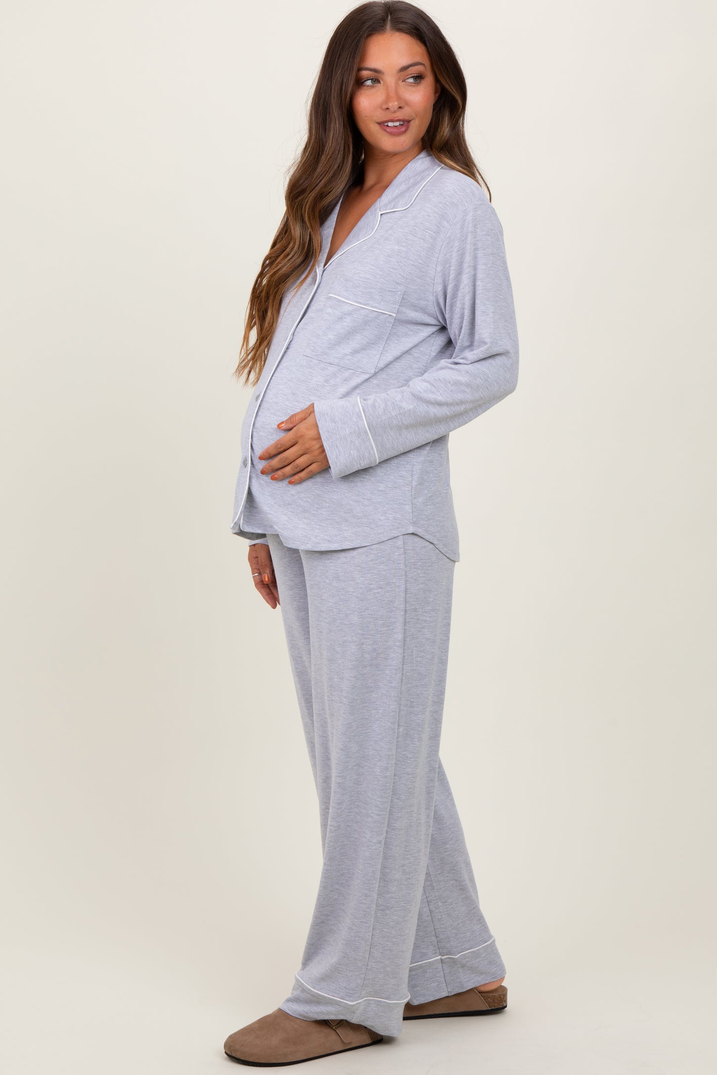 woman wearing a light gray maternity pajama set with a button-up top and loose pants, showing her baby bump