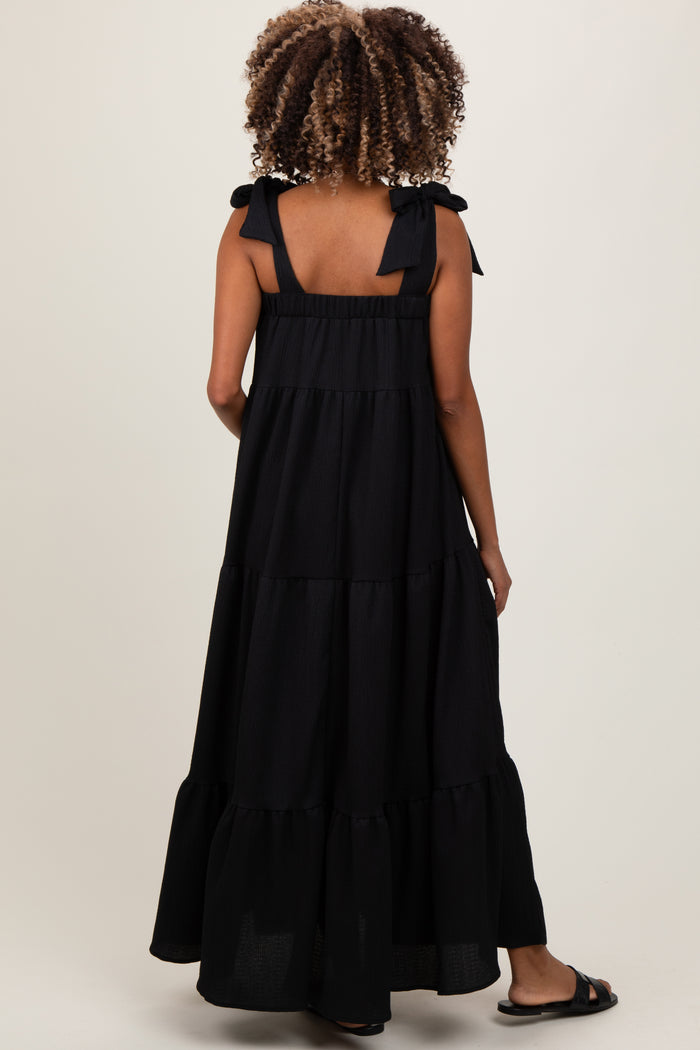 woman wearing a long black maternity dress with tiered design and bow straps, showing her pregnant belly from the back
