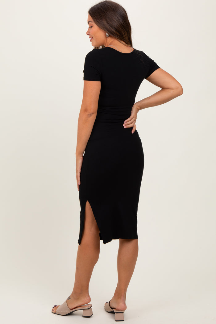 woman wearing a black short sleeve ribbed maternity dress with a side slit, showing her back and playful pose
