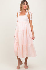 woman wearing a pink and white gingham maternity dress with tie straps and a tiered skirt, showcasing her baby bump