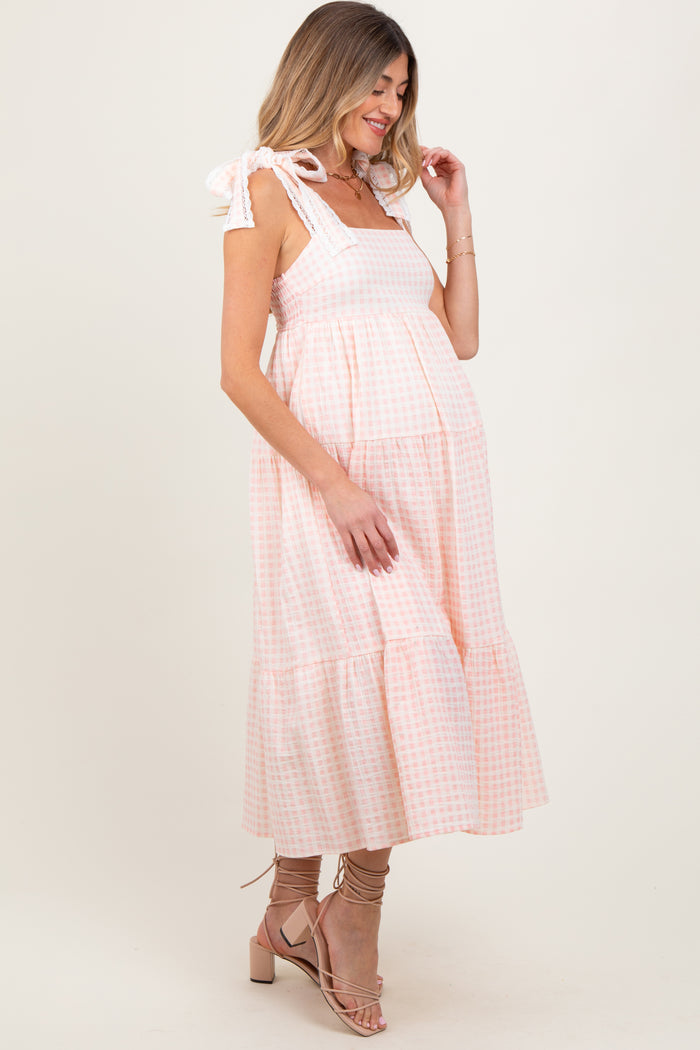 woman wearing a pink and white gingham maternity dress with tie straps and a flowing silhouette, showing baby bump