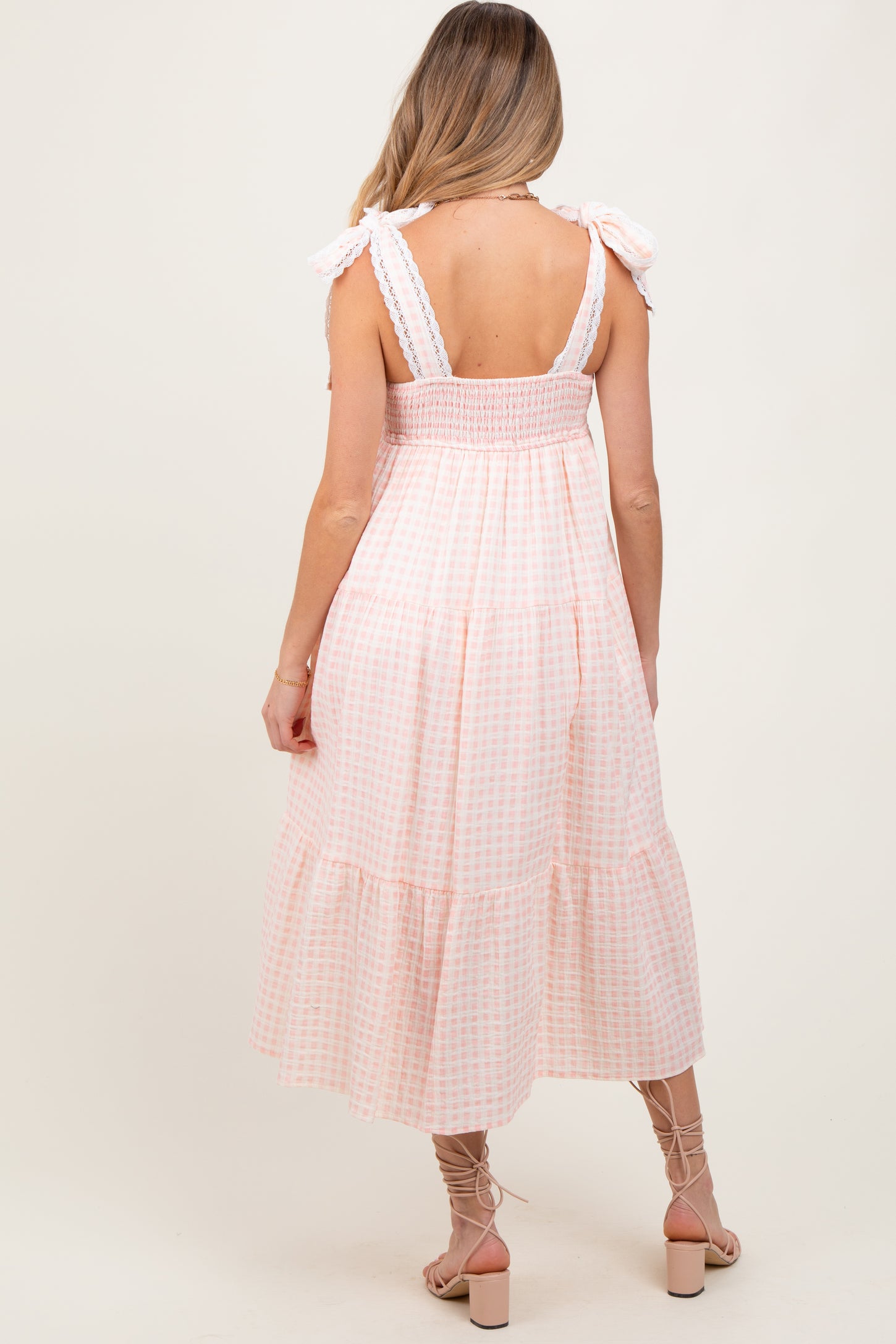 woman wearing a pink and white gingham maternity dress with smocked bodice and ruffled straps, showing her baby bump from the back