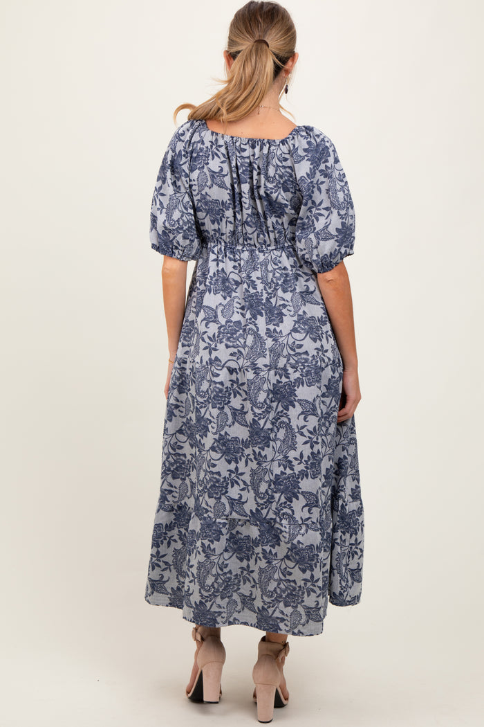 woman wearing a blue floral maternity maxi dress with puff sleeves, showcasing a flowing fit and gathered back detail