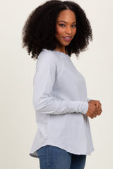 woman wearing a light gray long sleeve top with a curved hem and relaxed fit, standing sideways
