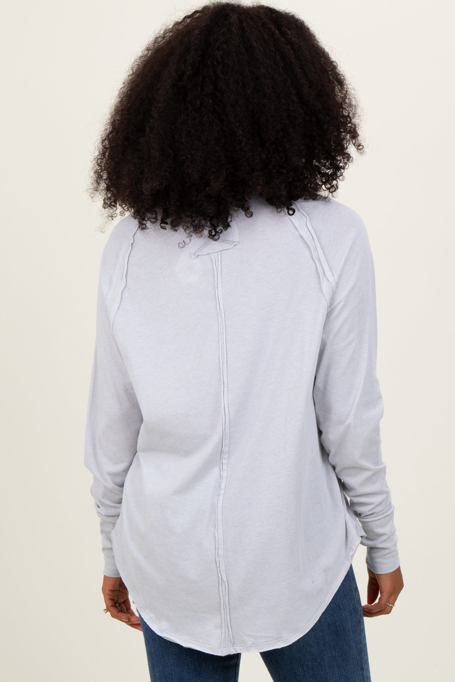 woman wearing a light gray long sleeve top with a rounded hem and button detail on the back