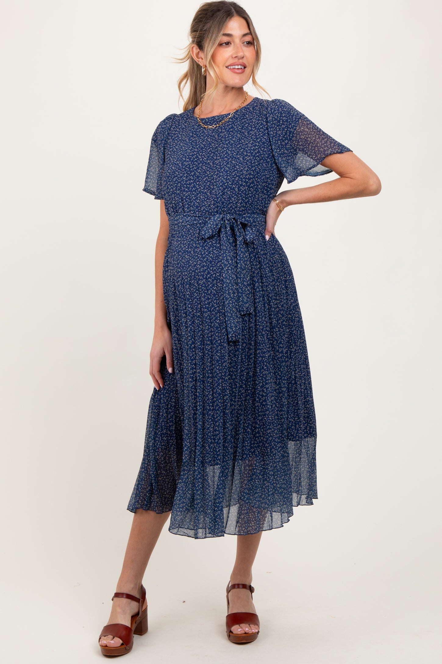 woman wearing a navy blue floral maternity dress with short sleeves and a waist tie, showcasing her baby bump