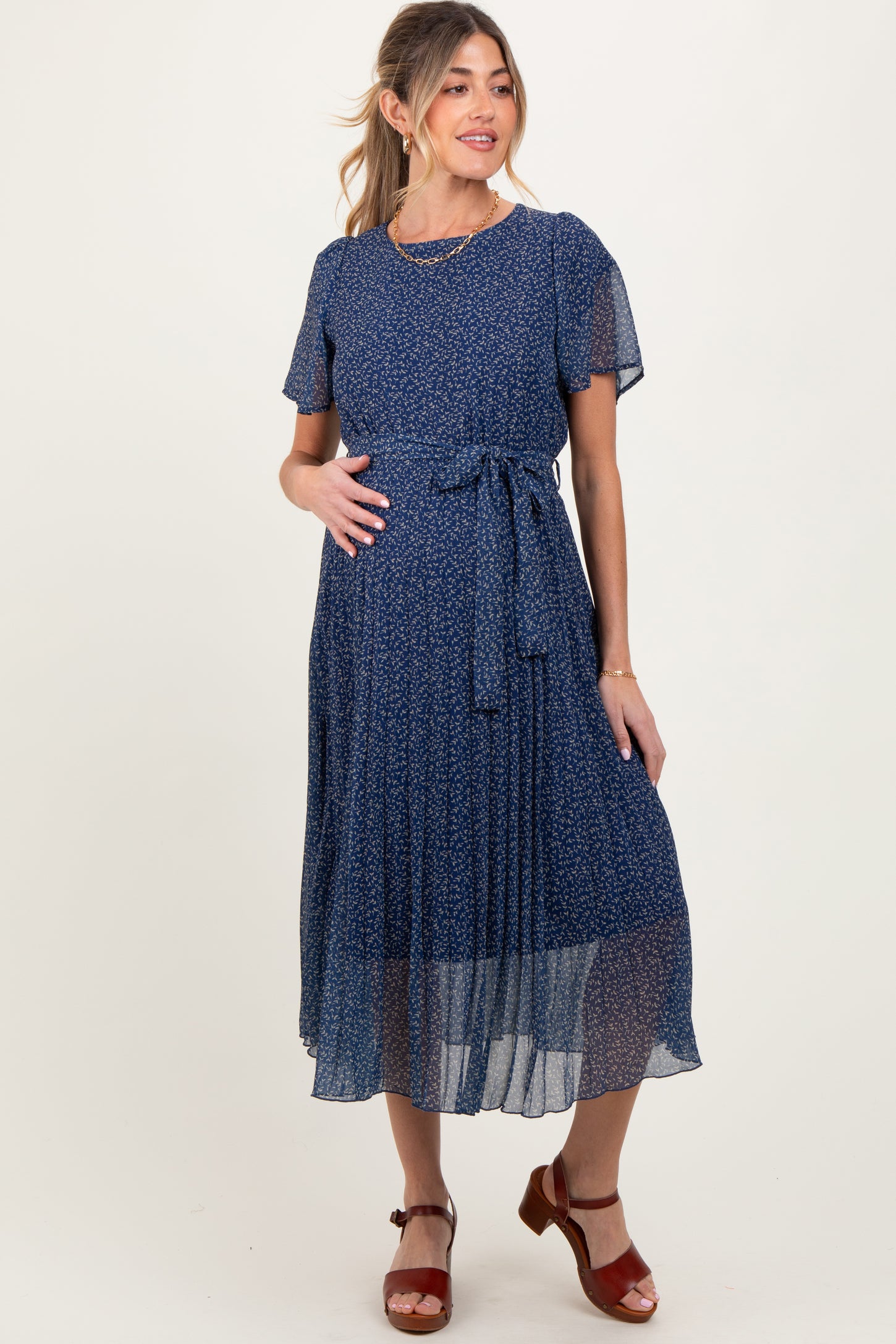 woman wearing a dark blue floral maternity dress with short sleeves and a tie belt, showing her baby bump