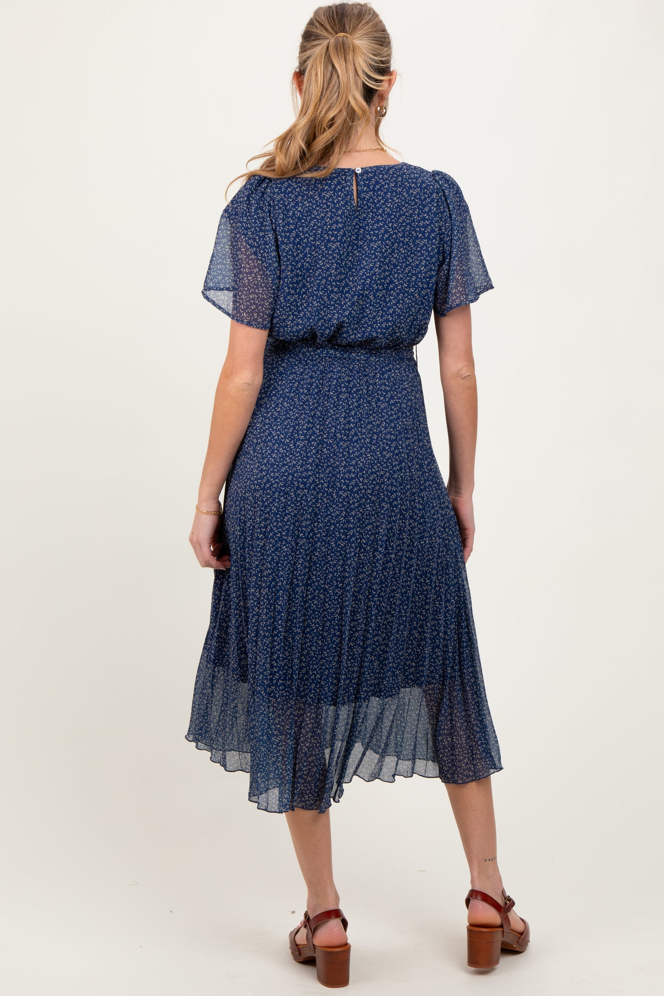 woman wearing a navy blue floral maternity dress with short sleeves and flowing skirt, showing a baby bump from the back