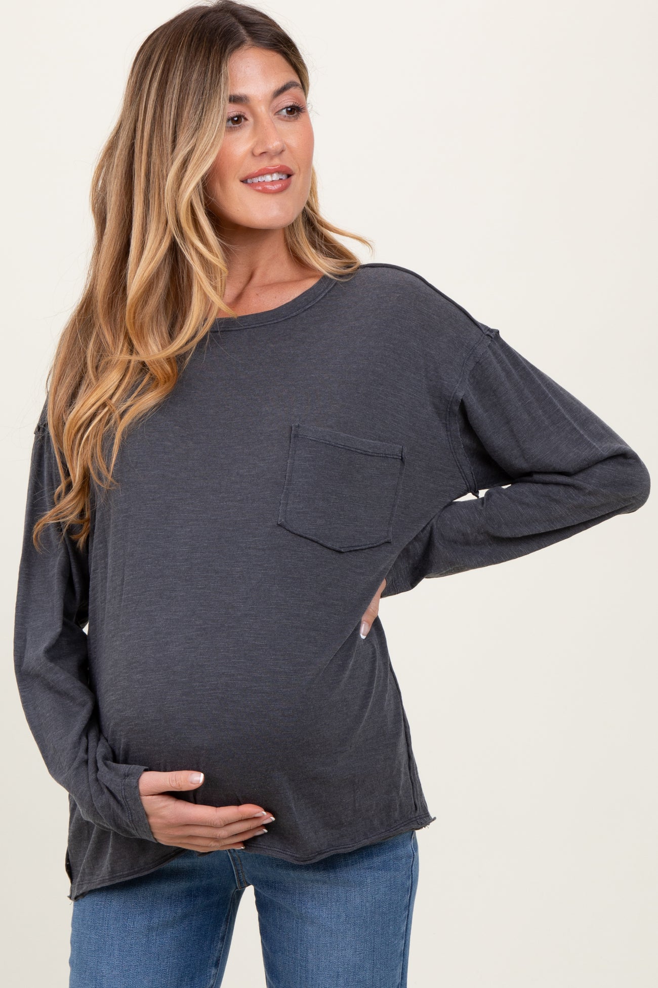 woman wearing a charcoal gray long sleeve maternity top, showing her baby bump while posing with one hand on her belly