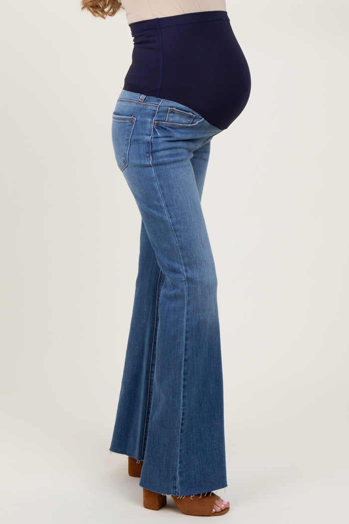 woman wearing a pair of light blue maternity flare jeans with a navy belly panel, highlighting a visible baby bump