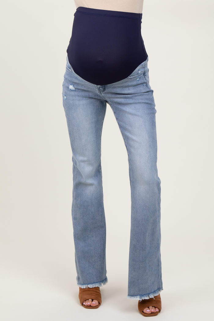 woman wearing maternity light wash flared jeans with a navy blue over-the-bump panel and brown heeled sandals