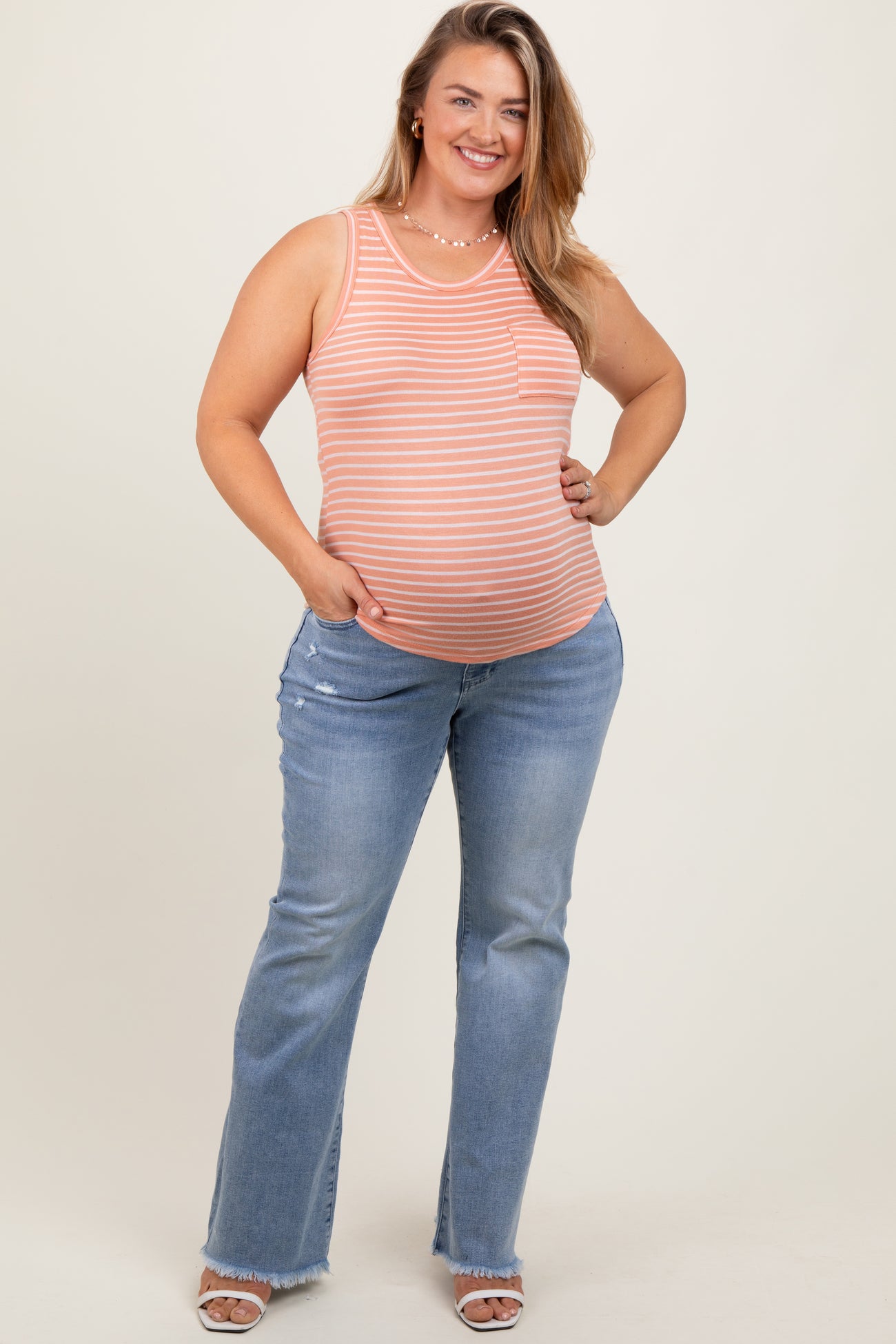 woman wearing a striped orange maternity tank top with a baby bump and flared light blue maternity jeans