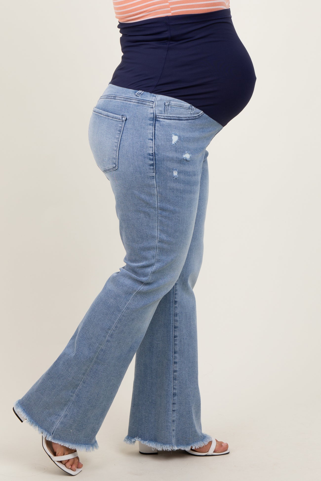 woman wearing light blue maternity plus flared jeans with a dark blue belly panel and a visible baby bump
