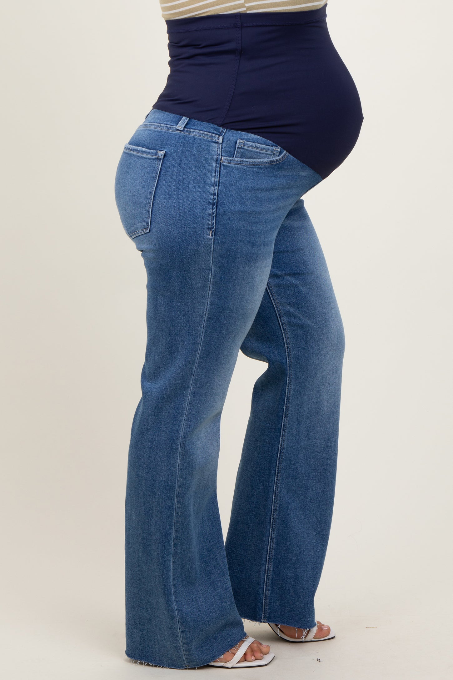 woman wearing a navy blue maternity tank top and blue flared maternity jeans, showing her baby bump
