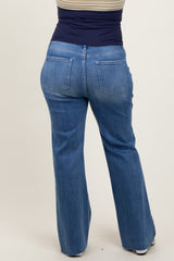 woman wearing a navy maternity plus top and blue flared maternity jeans, showing the back view of the jeans