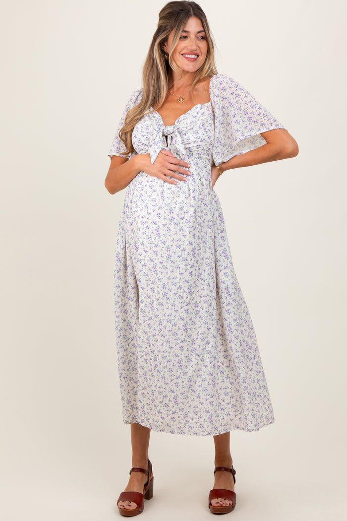 woman wearing a light purple floral maternity dress with short flutter sleeves and a tied front, showing her baby bump