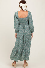 woman wearing a green floral maxi dress with puff sleeves and a smocked back, standing with her back to the camera