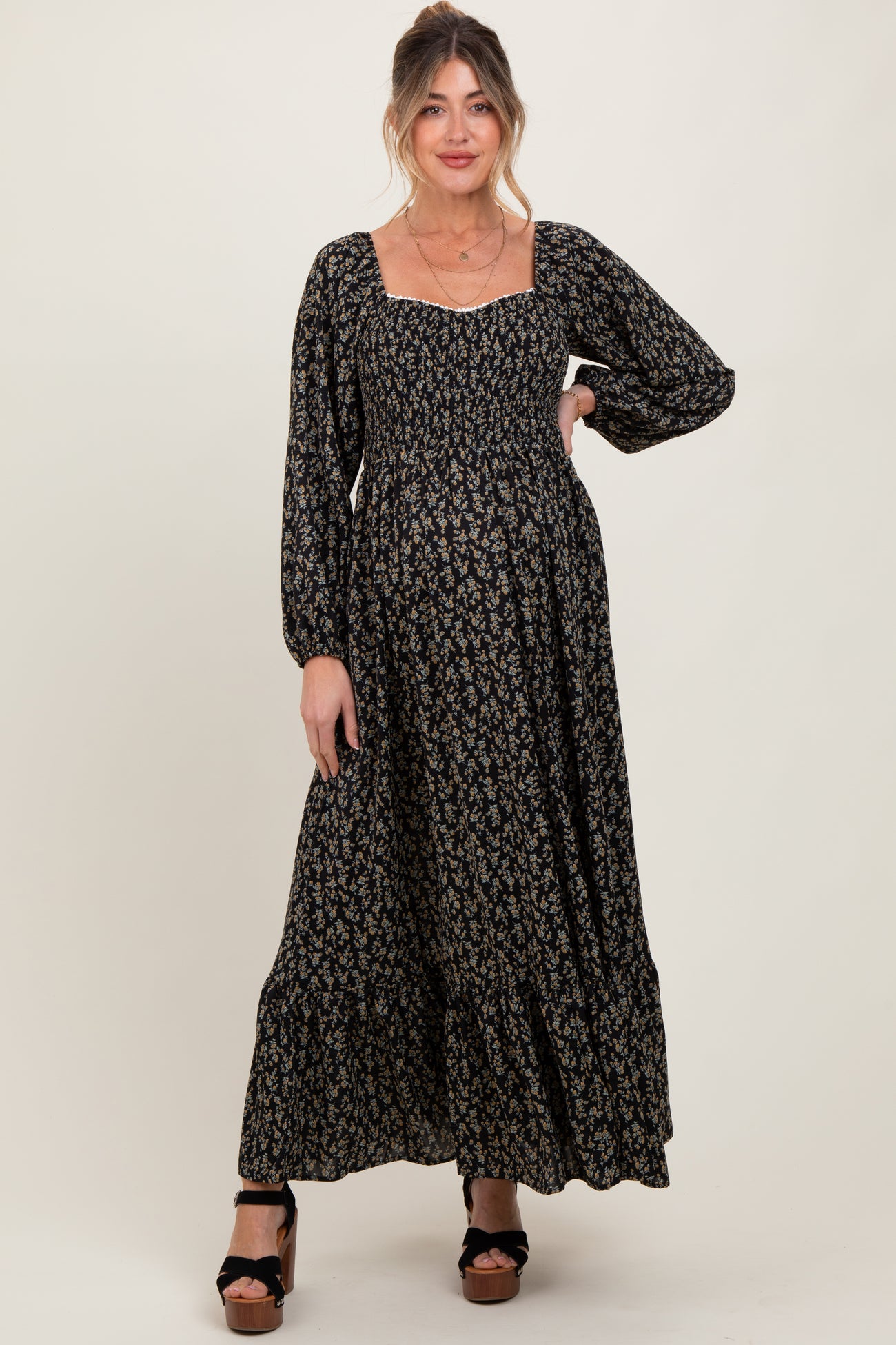 woman wearing a black floral print maternity maxi dress with long sleeves and a square neckline, showing a baby bump