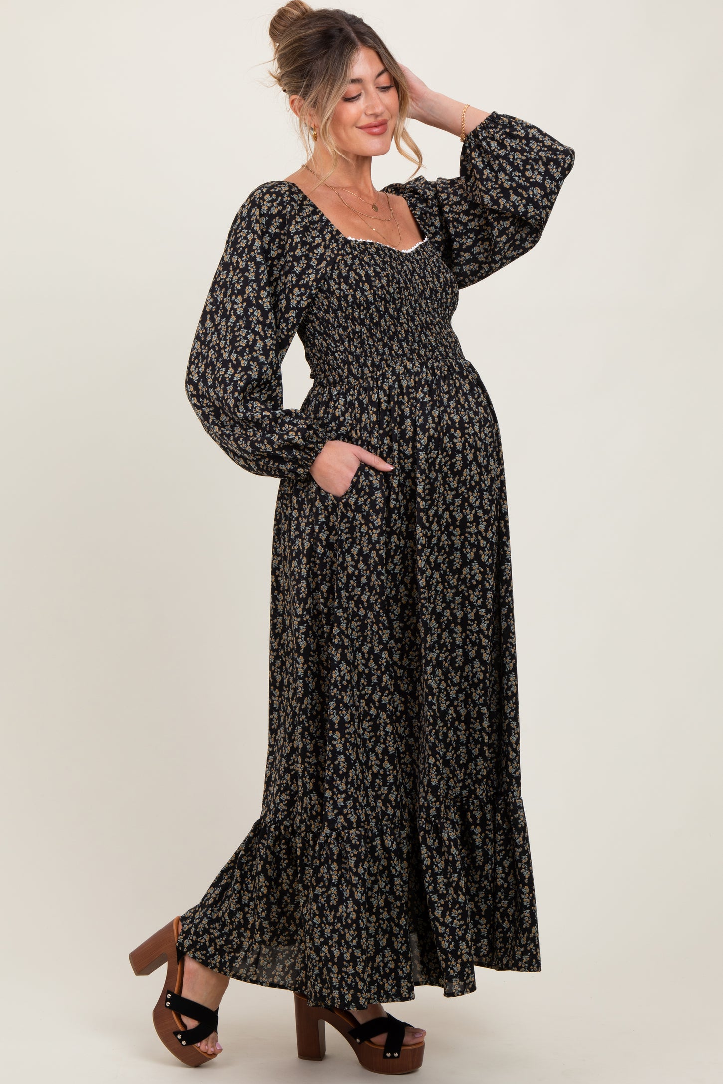woman wearing a black floral maternity maxi dress with smocked bodice and long puff sleeves, showing her baby bump