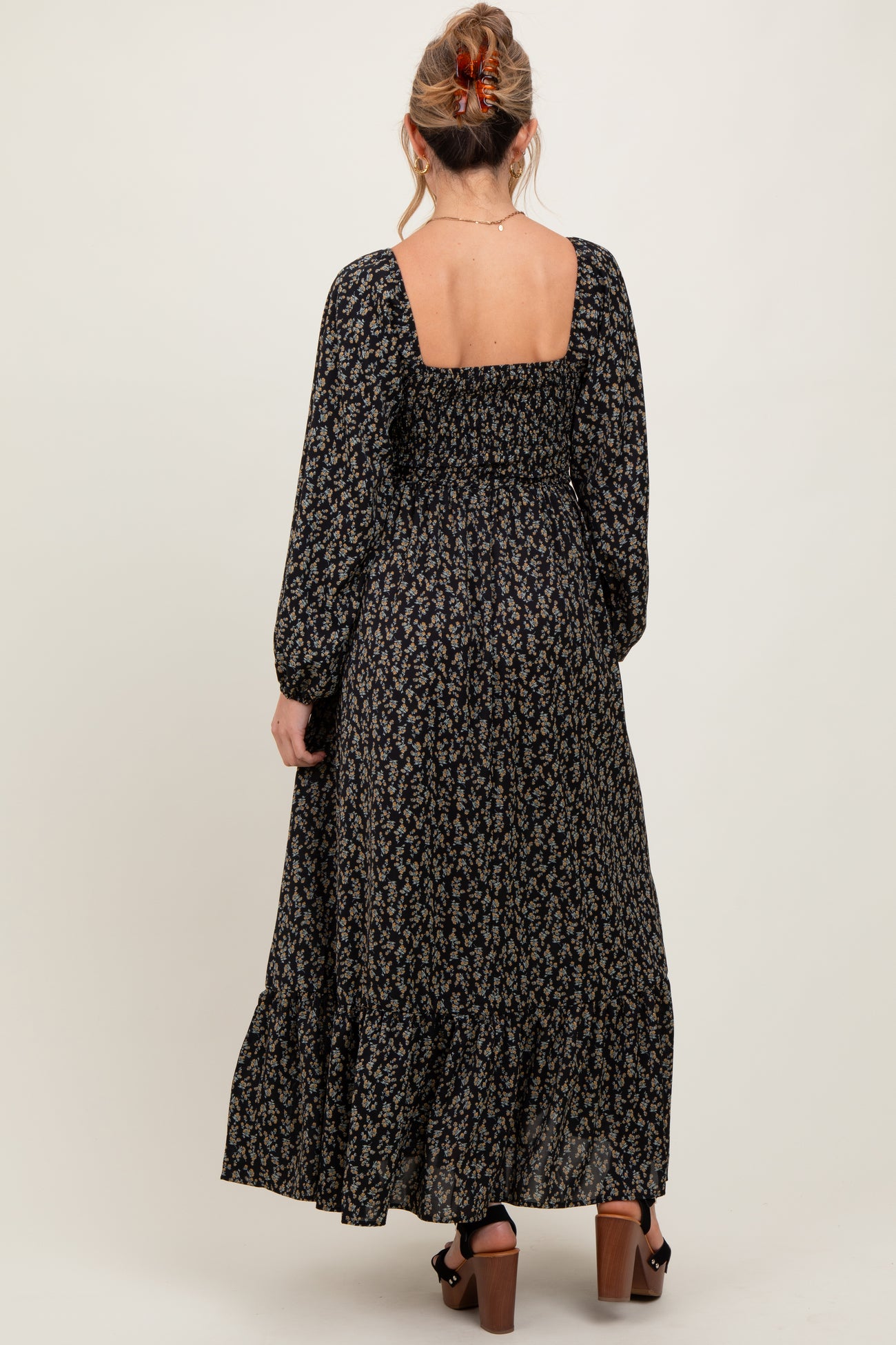 woman wearing a black floral maternity maxi dress with a square back and long sleeves, showing a baby bump