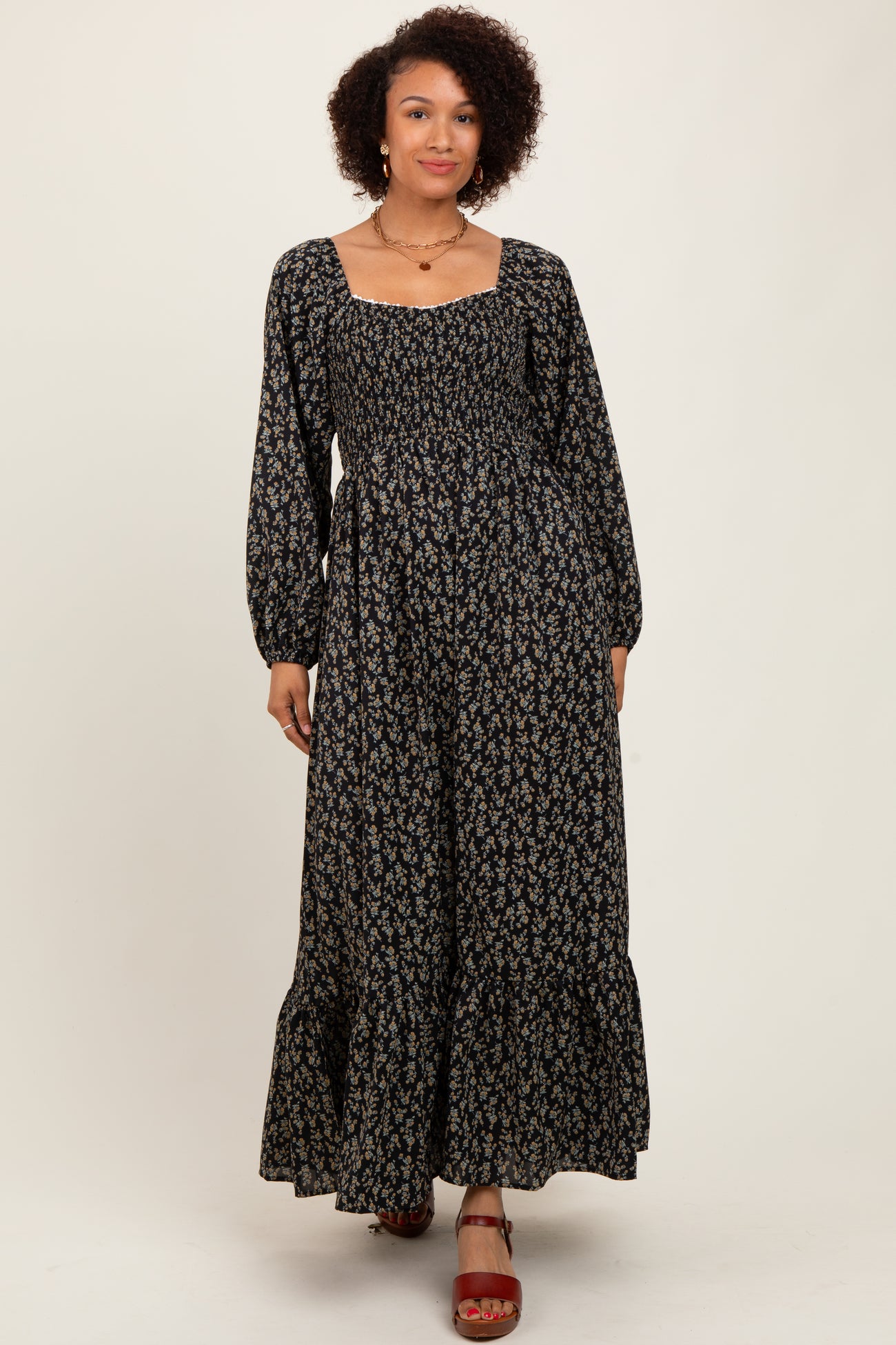 woman wearing a black floral maxi dress with long sleeves and a square neckline, standing on a neutral background