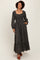 woman wearing a black floral long sleeve maxi dress with a square neckline and ruffle hem, standing with hands in pockets