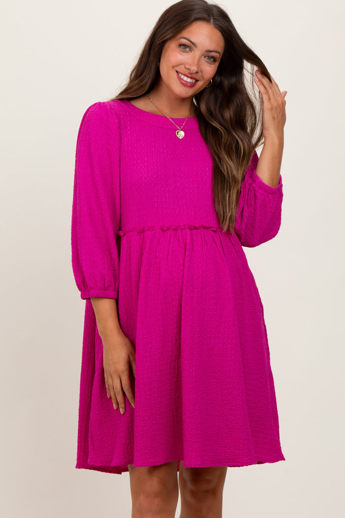 woman wearing a vibrant pink maternity dress with long puff sleeves and a relaxed fit, smiling and touching her hair
