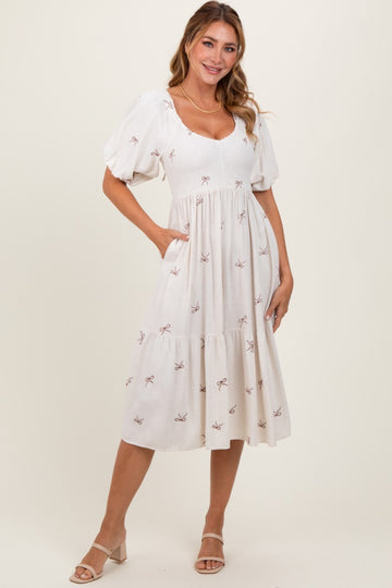 woman wearing a white midi dress with puff sleeves and bow embroidery, standing with hands in pockets