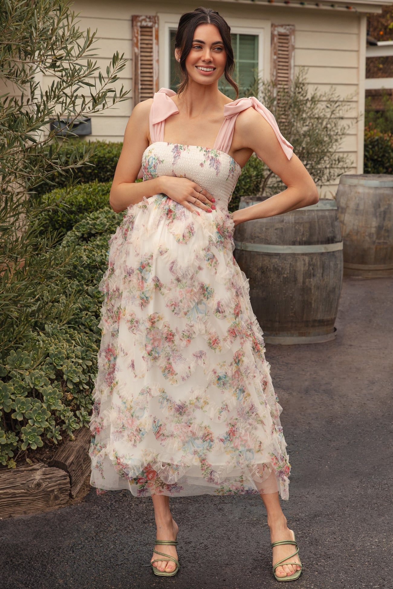 woman wearing a floral maternity dress with smocked bodice and pink shoulder ties, showing her baby bump