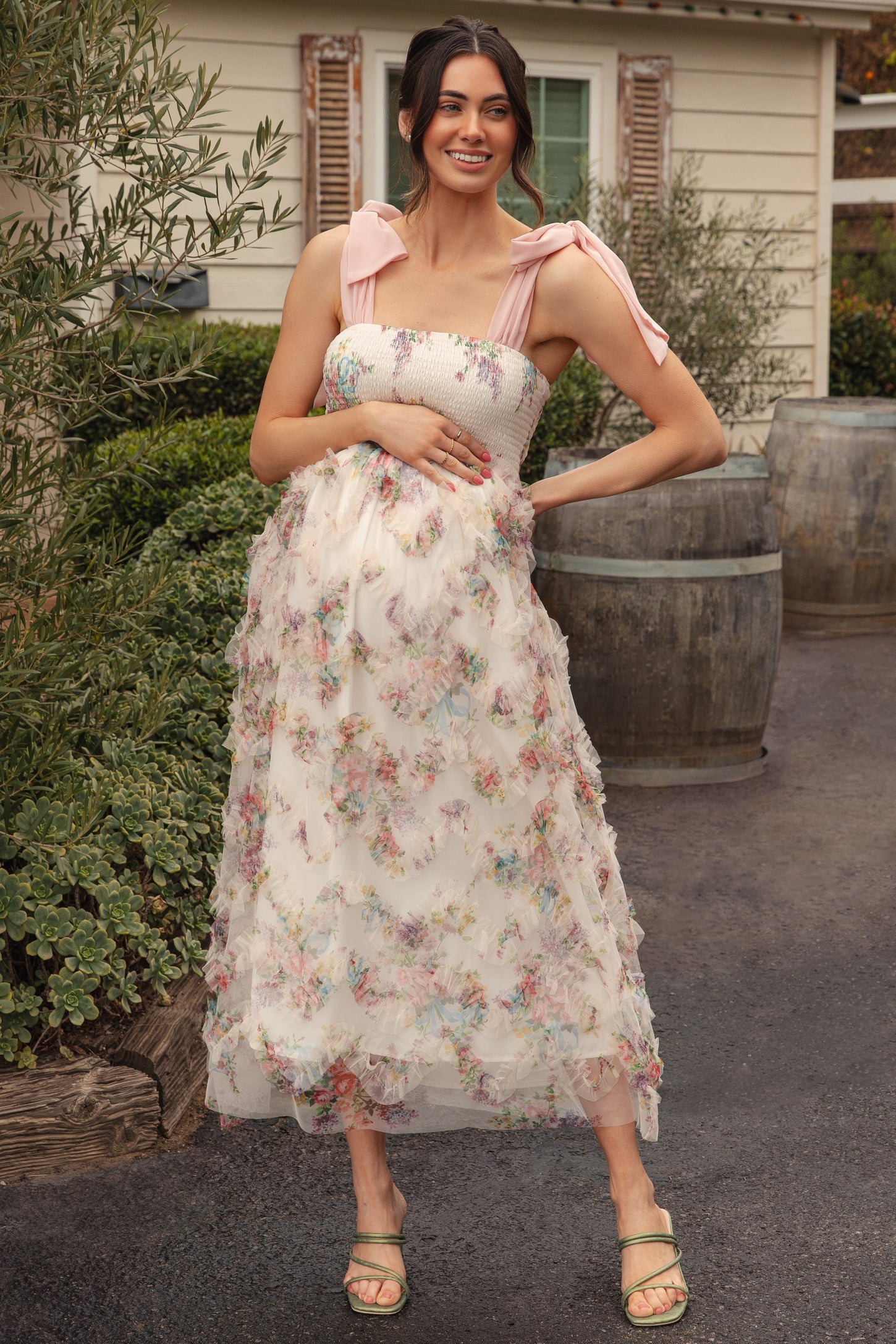 woman wearing a floral maternity dress with smocked bodice and pink shoulder ties, showing her baby bump