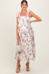 woman wearing a floral maternity dress with ruffled details and pink bow straps, holding a small bag and showing her baby bump