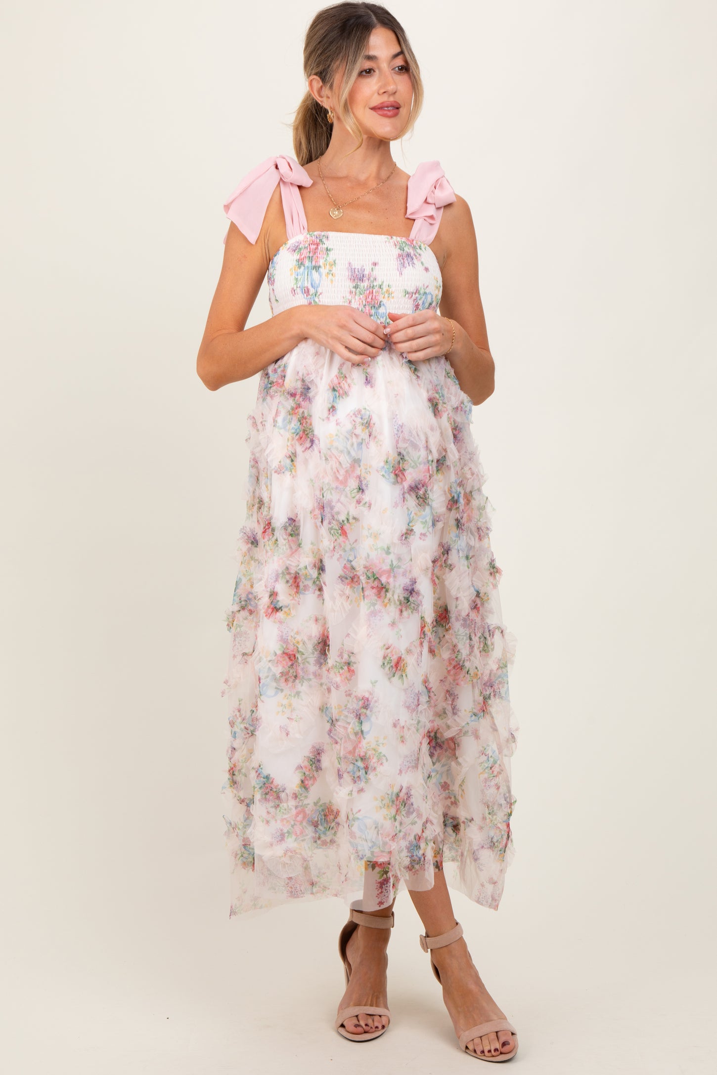 woman wearing a floral maternity dress with pink bow straps and tiered ruffles, showcasing a baby bump