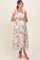 woman wearing a floral maternity dress with pink bow straps and tiered ruffles, showcasing a baby bump