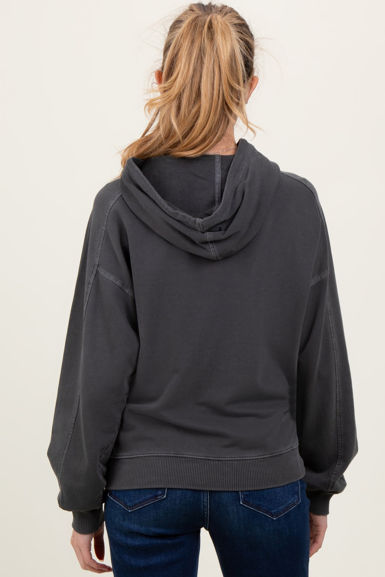 woman wearing a dark gray maternity hoodie, view from the back, with a relaxed fit and hooded design