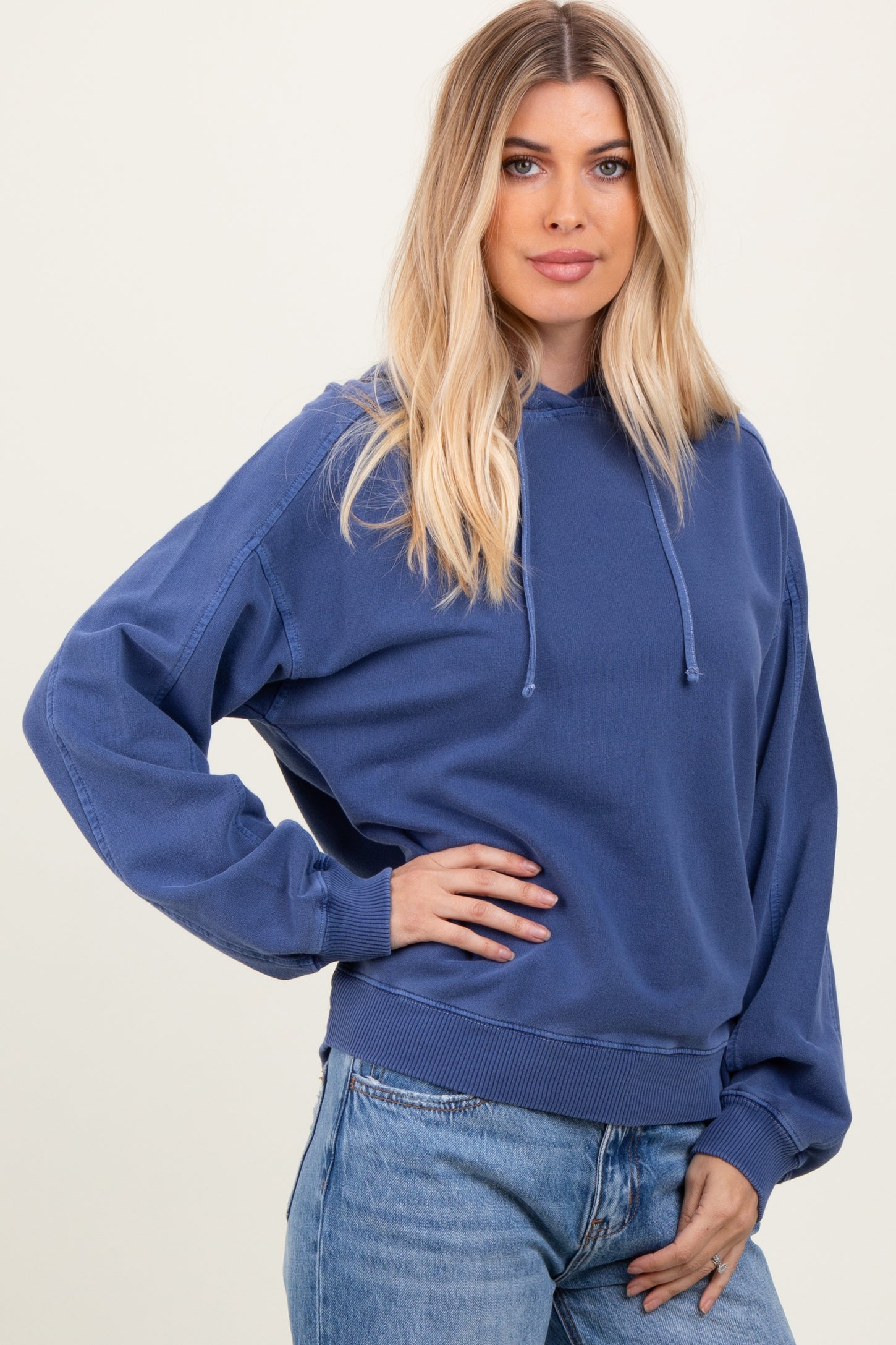 woman wearing a loose-fitting blue hoodie with a high neckline and long sleeves, paired with jeans