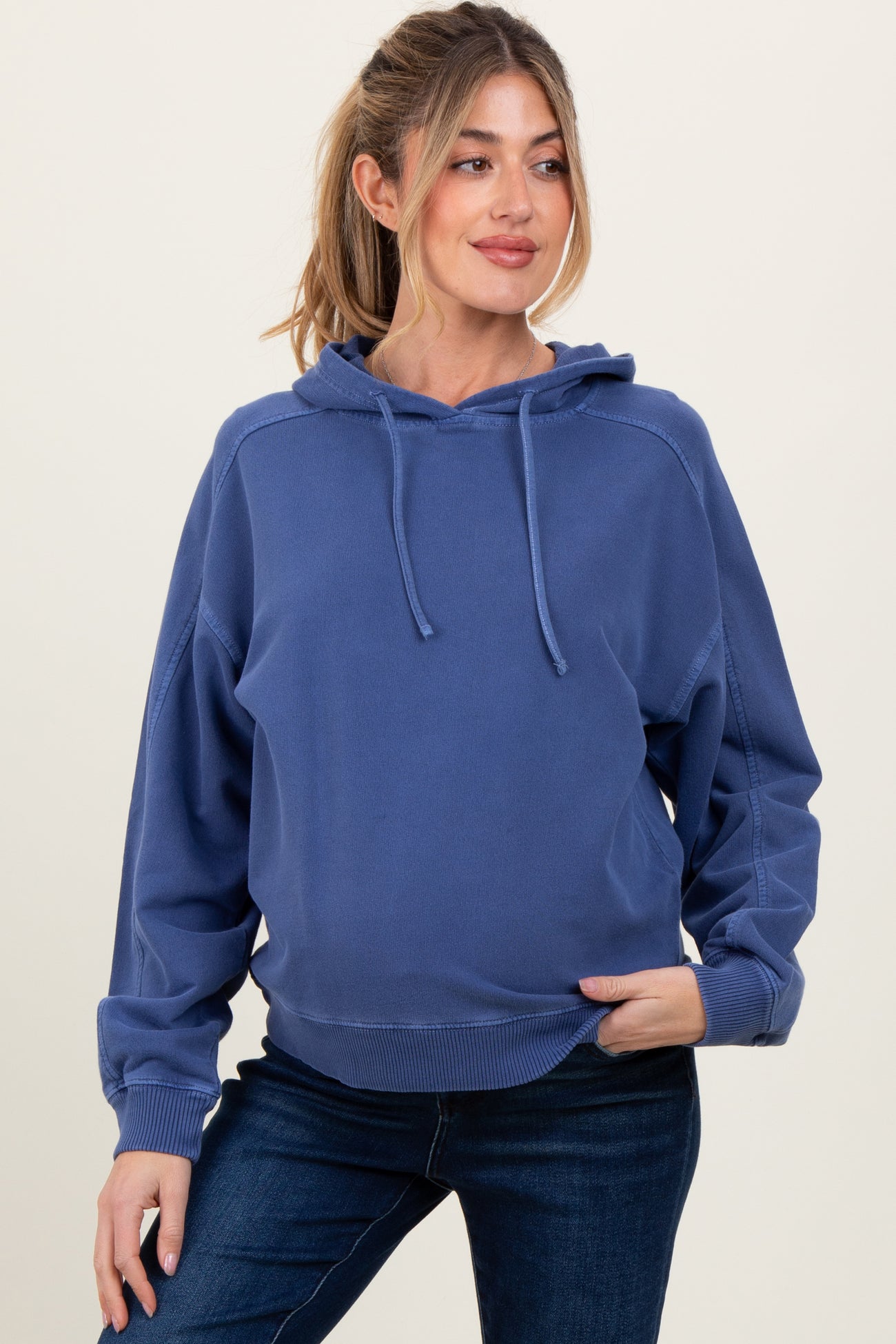 woman wearing a dark blue maternity hoodie with a relaxed fit and drawstring hood, paired with dark jeans