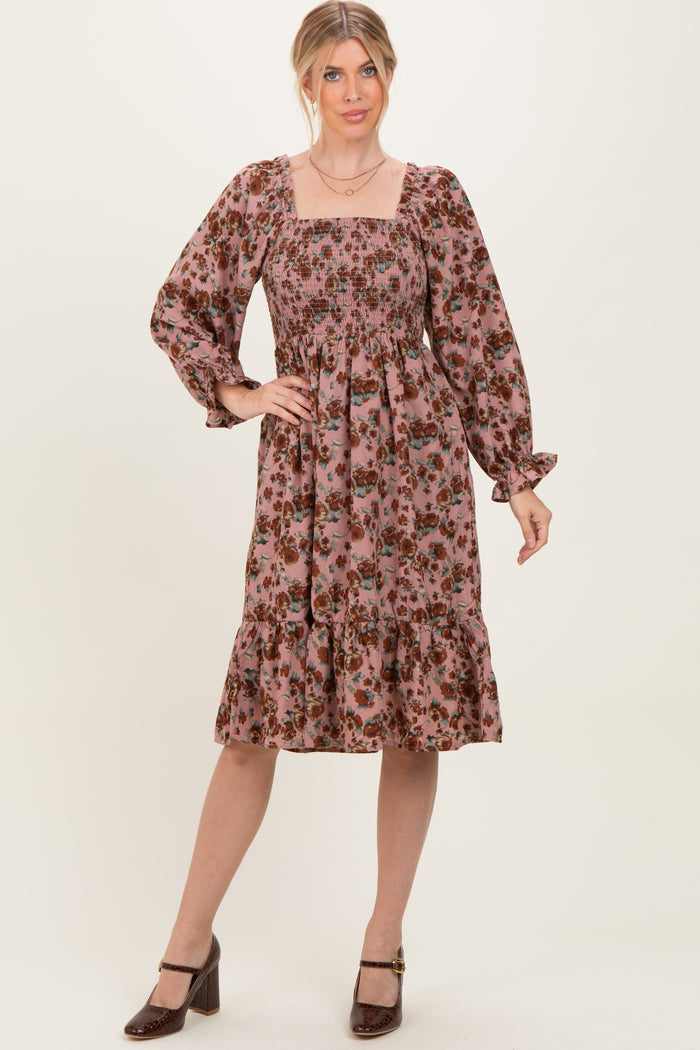 woman wearing a floral pink midi dress with smocked bodice and long sleeves, standing with one hand on her hip