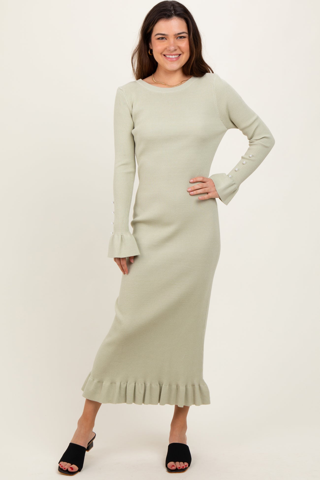 woman wearing a light green ribbed midi dress with ruffle hem and bell sleeves, standing and smiling.