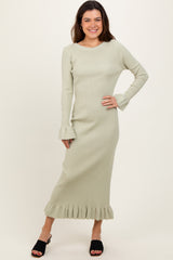 woman wearing a light green ribbed midi dress with ruffle hem and bell sleeves, standing and smiling.