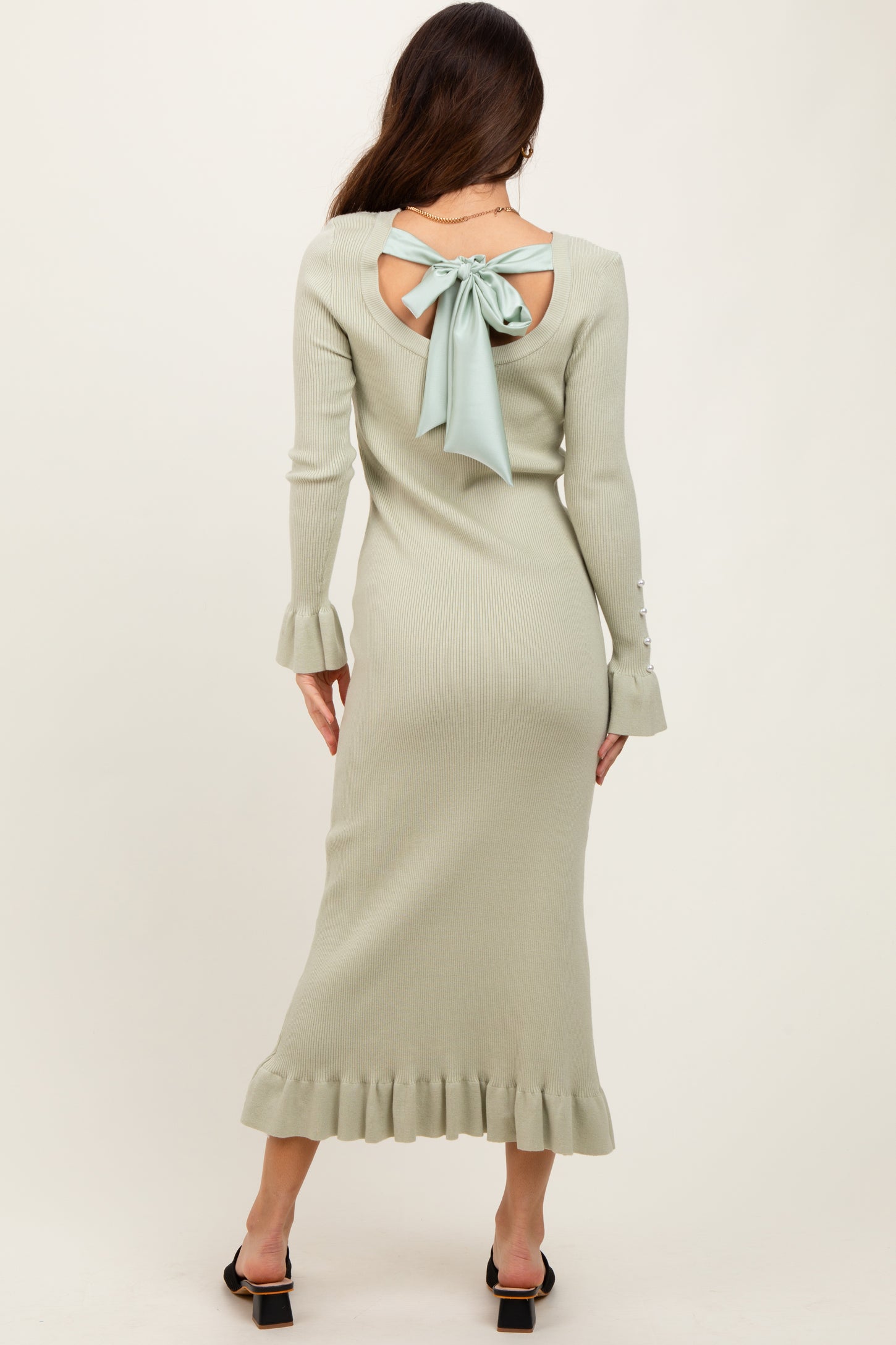 woman wearing a light green ribbed midi dress with a bow detail at the back and ruffled hem