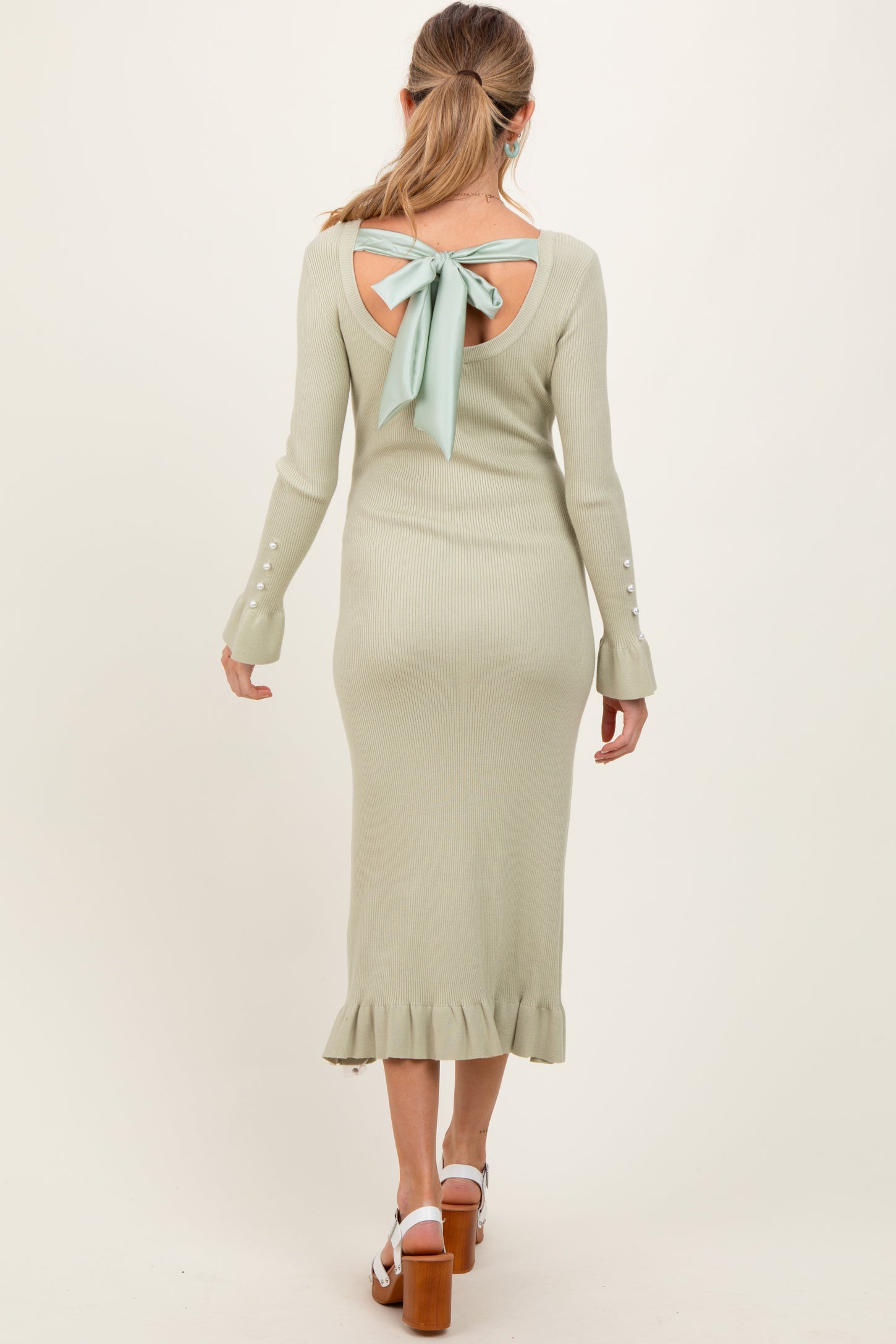 woman wearing a light green long sleeve maternity dress with an open back and bow detail, featuring a ruffle hem