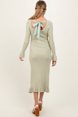 woman wearing a light green long sleeve maternity dress with an open back and bow detail, featuring a ruffle hem