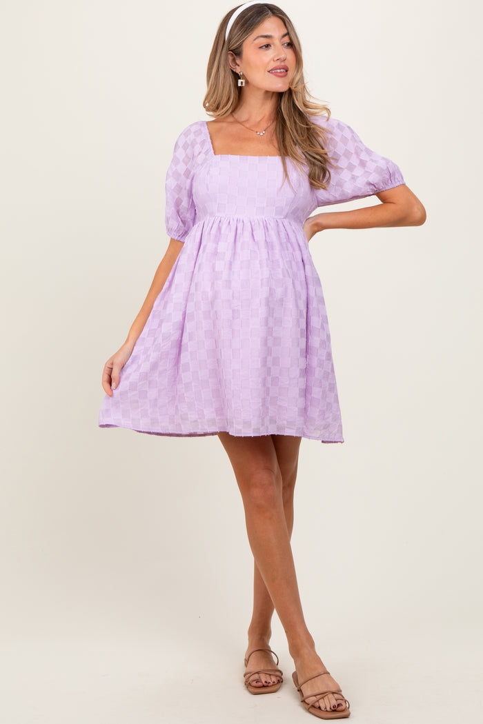 woman wearing a lavender maternity dress with a square neckline and puff sleeves, standing in a playful pose