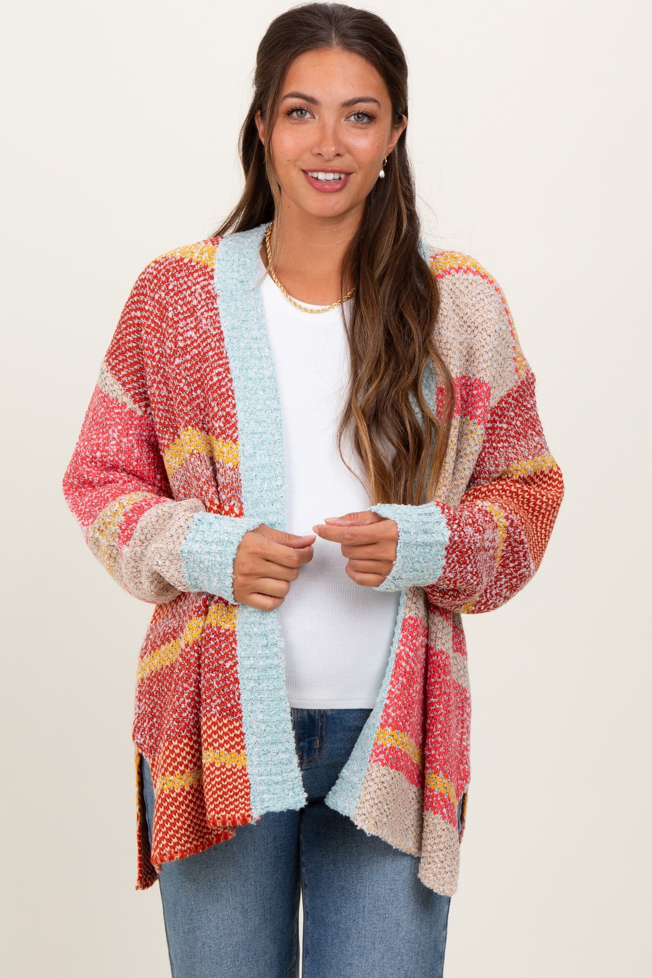 woman wearing a multicolor striped open-front maternity cardigan over a white top and jeans, holding the edges of the cardigan
