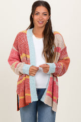 woman wearing a multicolor striped open-front maternity cardigan over a white top and jeans, holding the edges of the cardigan