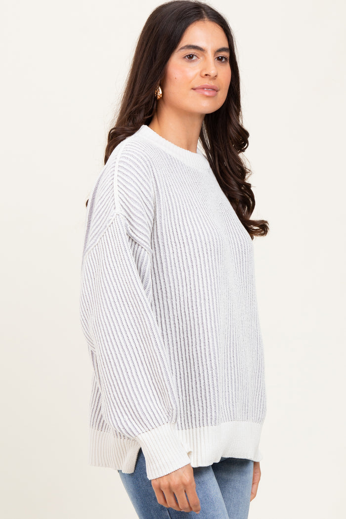 woman wearing a light gray oversized ribbed sweater with a white hem and cuffs, paired with blue jeans