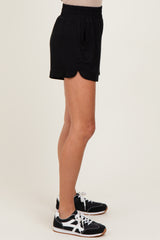 woman wearing black scalloped hem athletic shorts and black sneakers, standing sideways against a light background