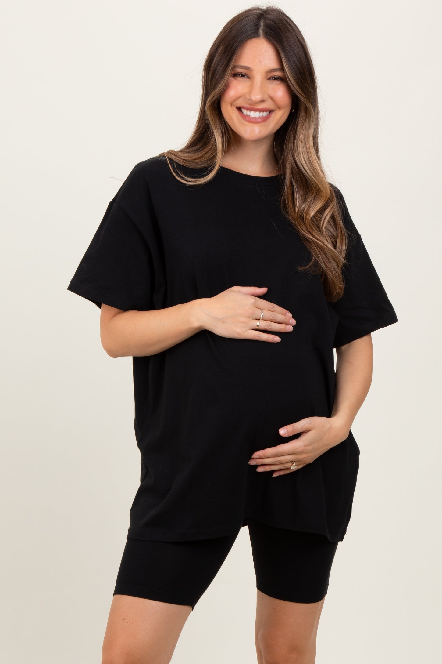 woman wearing a black oversized maternity t-shirt and black biker shorts, holding her baby bump