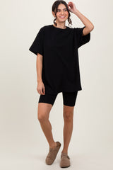woman wearing a black oversized t-shirt and black bike shorts, standing and smiling with one hand in her hair