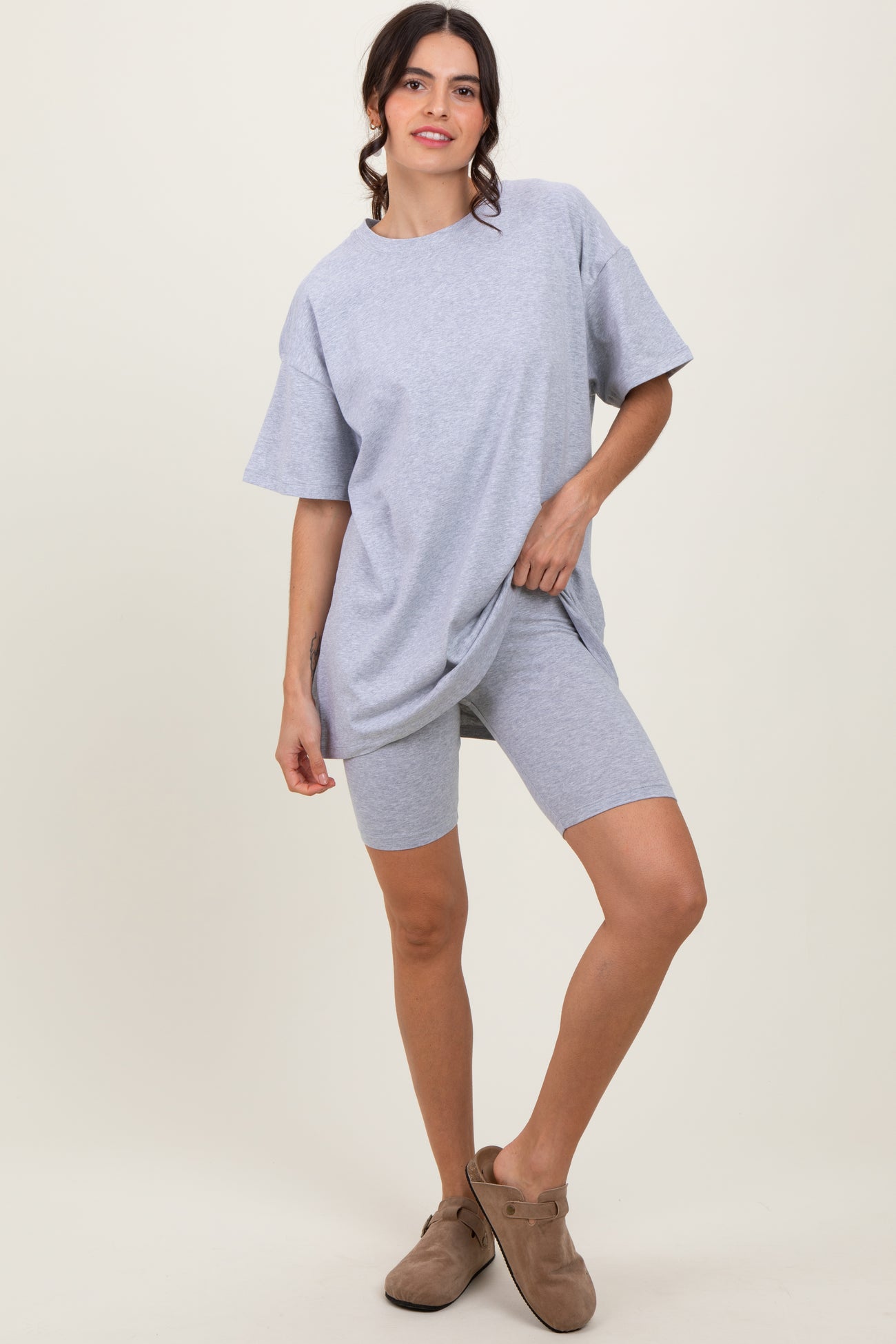 woman wearing a light gray oversized t-shirt and matching bike shorts, posing with one hand on her hip